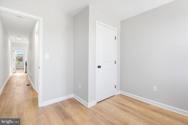 hallway featuring baseboards, light wood finished floors, and visible vents