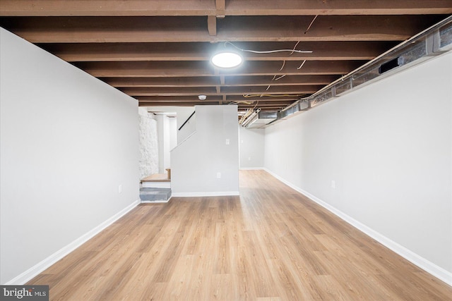 finished below grade area with baseboards, wood finished floors, and stairway