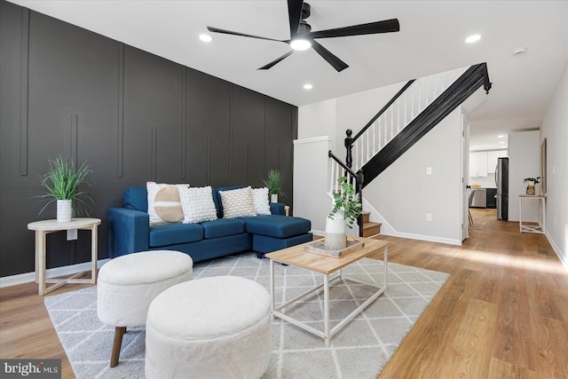 living room featuring light wood-type flooring, baseboards, ceiling fan, and stairway
