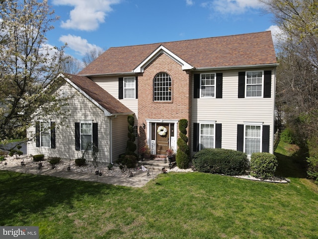 colonial home with brick siding, a shingled roof, and a front yard