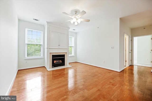 unfurnished living room featuring light wood finished floors, a ceiling fan, baseboards, a fireplace with flush hearth, and visible vents