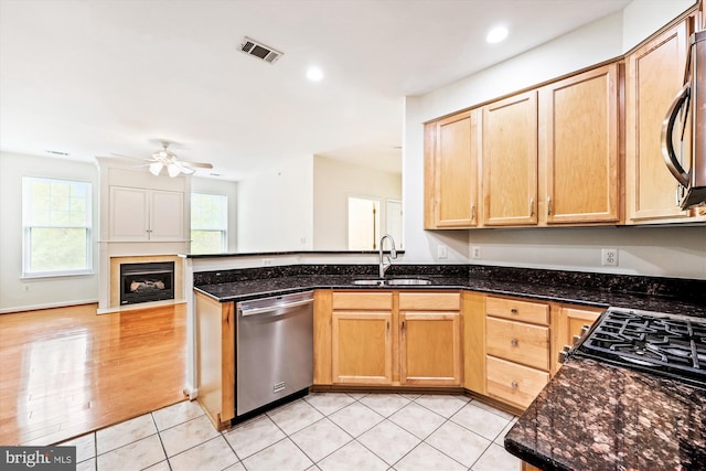 kitchen with ceiling fan, stainless steel dishwasher, a sink, a peninsula, and dark stone countertops