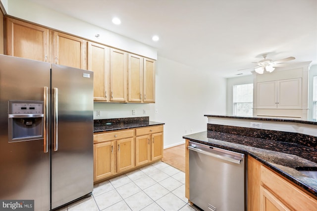 kitchen featuring light tile patterned floors, appliances with stainless steel finishes, a ceiling fan, and dark stone countertops