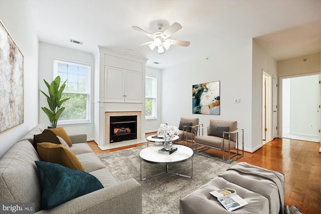 living area with ceiling fan, visible vents, a fireplace with flush hearth, wood finished floors, and baseboards