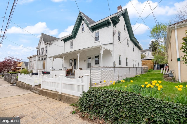 view of front of house with stucco siding, a chimney, covered porch, and a fenced front yard