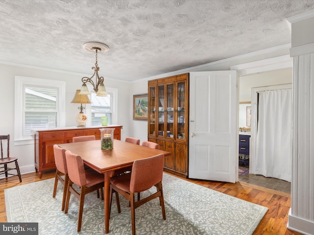 dining space with a textured ceiling, light wood-style floors, and crown molding