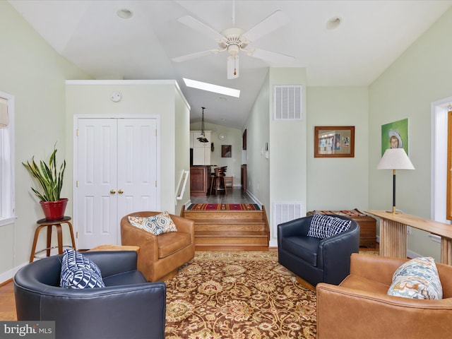 living room featuring ceiling fan, baseboards, vaulted ceiling with skylight, and visible vents