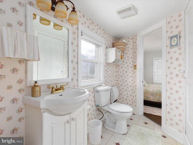 ensuite bathroom featuring wallpapered walls, tile patterned flooring, visible vents, toilet, and vanity