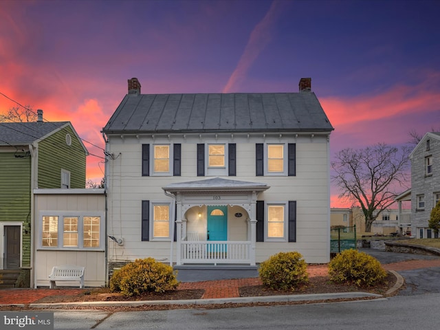 colonial-style house featuring metal roof, a standing seam roof, a chimney, and covered porch