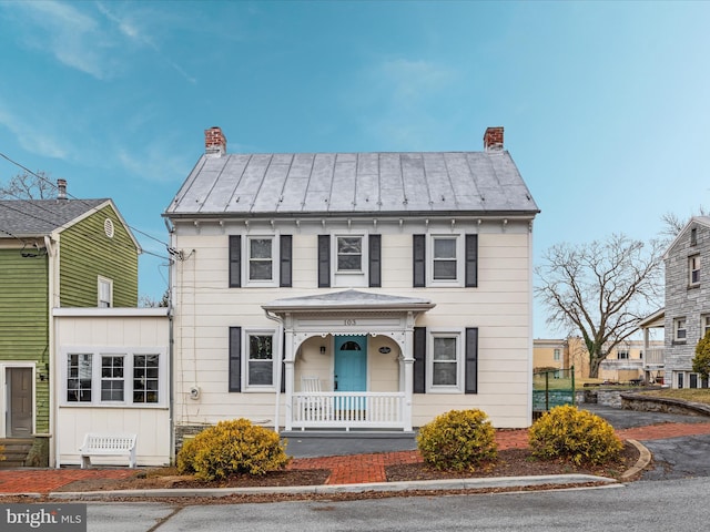 view of front of home featuring a standing seam roof, a chimney, covered porch, and metal roof