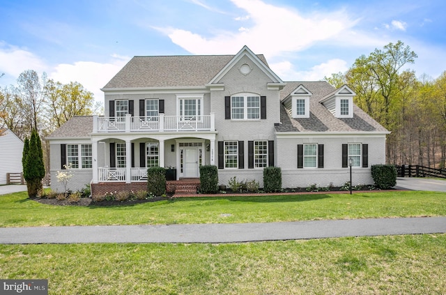 view of front of property featuring a balcony, roof with shingles, covered porch, a front lawn, and brick siding