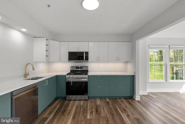 kitchen featuring a sink, stainless steel appliances, baseboards, green cabinetry, and dark wood-type flooring