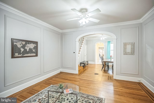 foyer featuring a decorative wall, arched walkways, crown molding, ceiling fan, and light wood finished floors