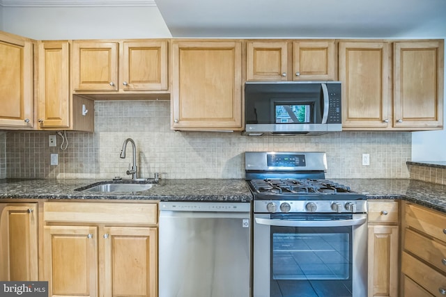 kitchen with appliances with stainless steel finishes, a sink, decorative backsplash, and dark stone counters