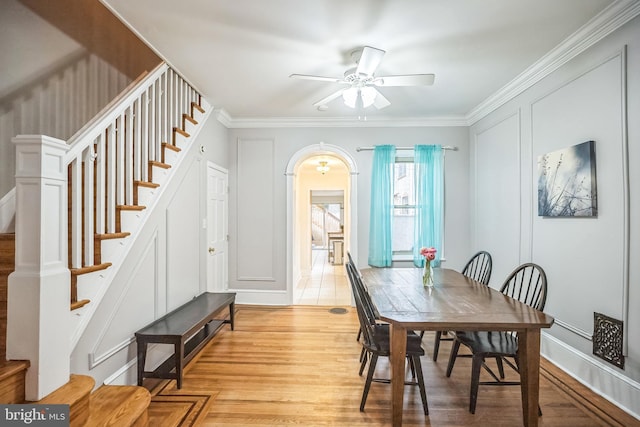 dining room with a ceiling fan, stairs, light wood-style floors, arched walkways, and crown molding