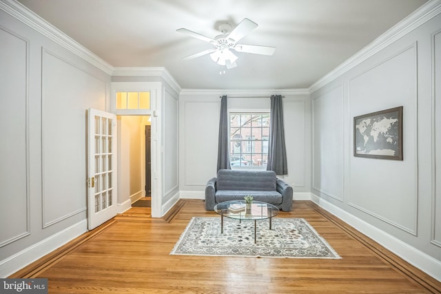 sitting room with a decorative wall, light wood-type flooring, ornamental molding, and a ceiling fan