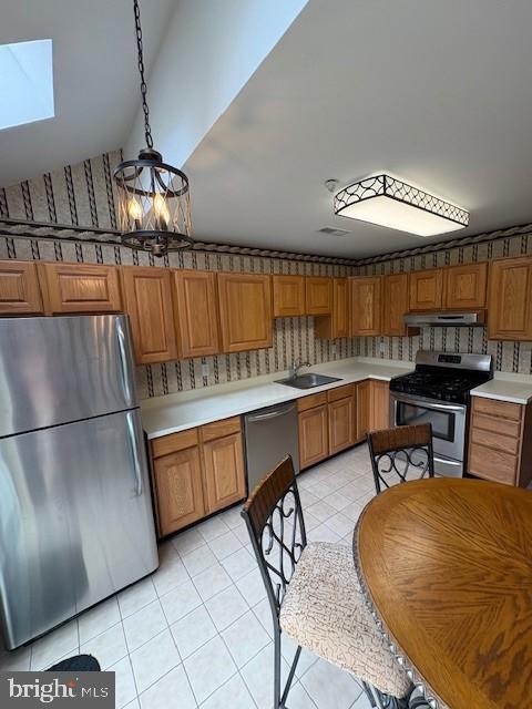 kitchen featuring stainless steel appliances, light countertops, light tile patterned floors, brown cabinetry, and vaulted ceiling