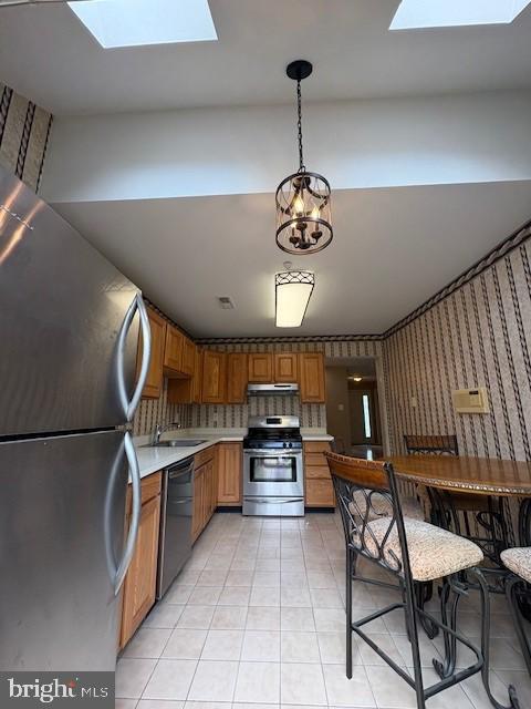 kitchen with stainless steel appliances, a skylight, a sink, light countertops, and wallpapered walls