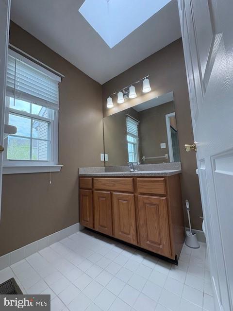 bathroom featuring a skylight, vanity, baseboards, and tile patterned floors