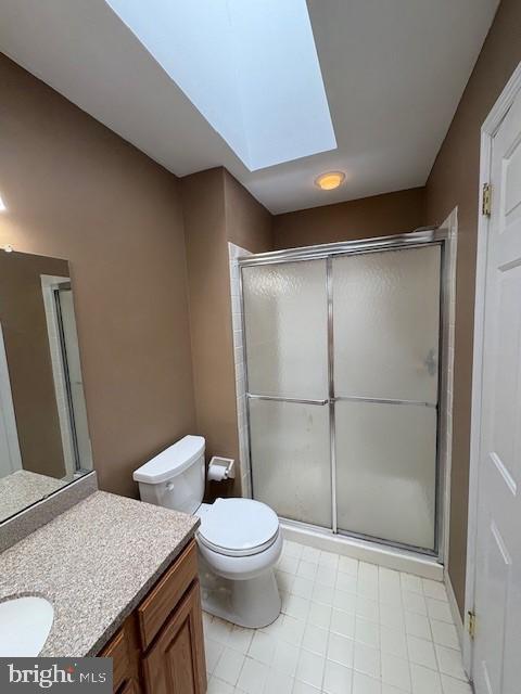 full bathroom with a skylight, a shower with shower door, toilet, and vanity