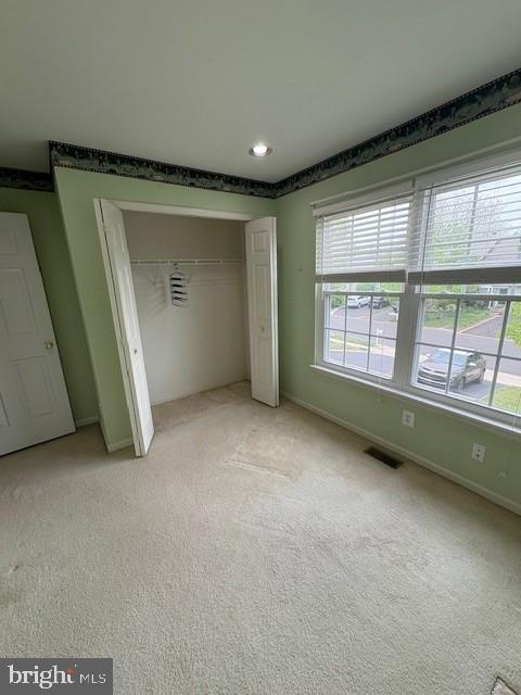 unfurnished bedroom featuring multiple windows, light colored carpet, a closet, and baseboards