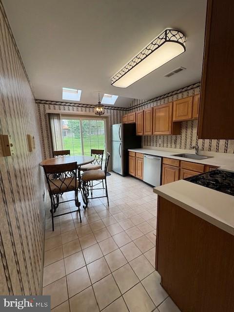 kitchen featuring stainless steel dishwasher, freestanding refrigerator, a sink, a skylight, and wallpapered walls