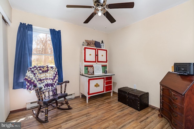 sitting room featuring baseboards, a ceiling fan, wood finished floors, and a baseboard radiator