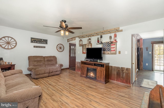 living room featuring baseboards, a ceiling fan, a glass covered fireplace, and light wood-style flooring