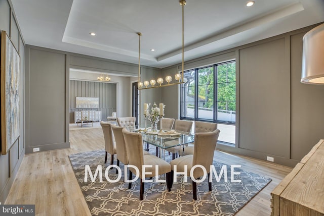 dining area with light wood finished floors, a chandelier, a raised ceiling, and a decorative wall