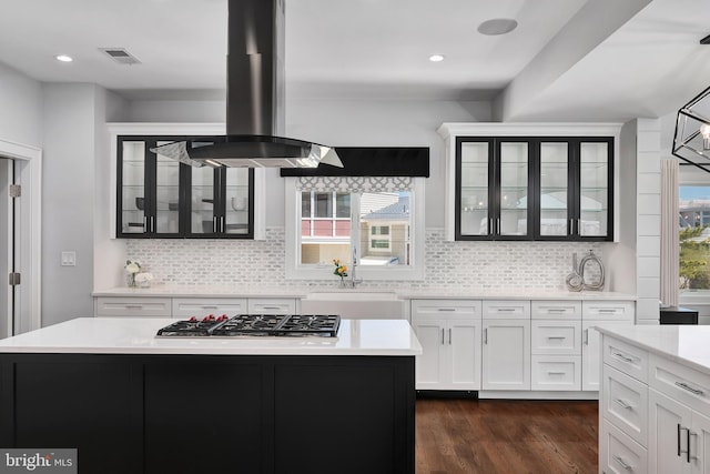 kitchen featuring a sink, stainless steel gas cooktop, island exhaust hood, light countertops, and visible vents