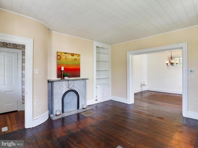 unfurnished living room with ornamental molding, built in features, hardwood / wood-style floors, baseboards, and a chandelier