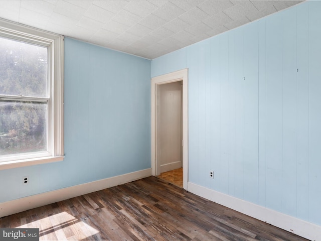 spare room featuring baseboards, dark wood finished floors, and a wealth of natural light