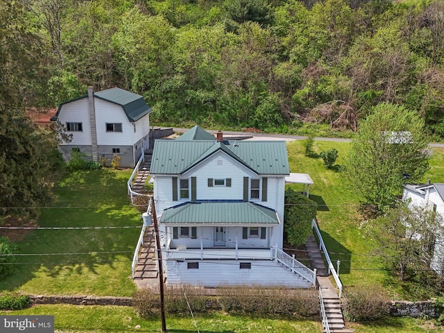 view of front of house with stairway, a wooded view, metal roof, and a front lawn