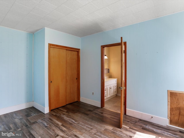 unfurnished bedroom featuring a closet, connected bathroom, dark wood-style flooring, and baseboards