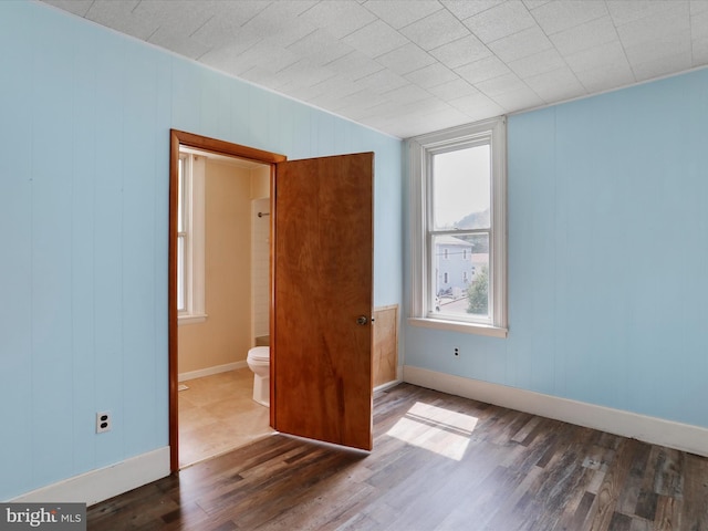 unfurnished bedroom featuring baseboards, connected bathroom, and wood finished floors
