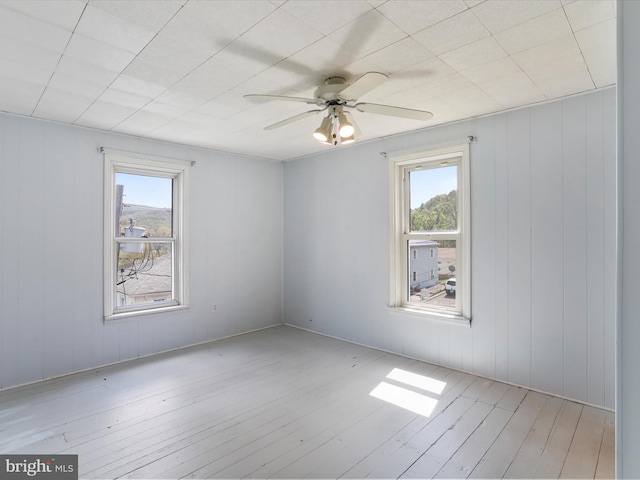 unfurnished room featuring a ceiling fan, wood finished floors, a wealth of natural light, and wood walls