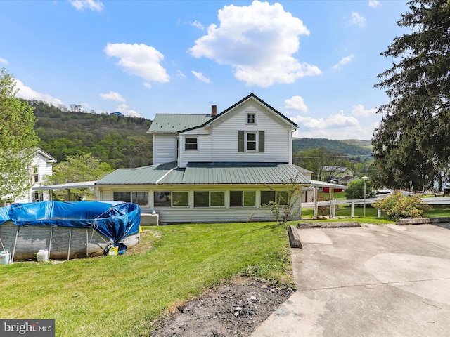 back of property with a lawn, metal roof, a covered pool, and a chimney