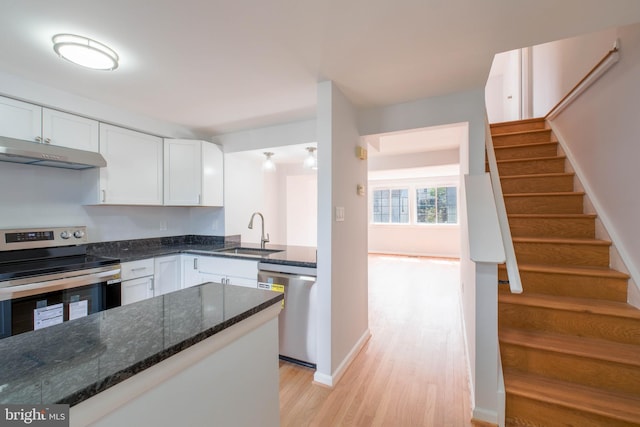 kitchen featuring white cabinets, under cabinet range hood, stainless steel appliances, a sink, and light wood-type flooring