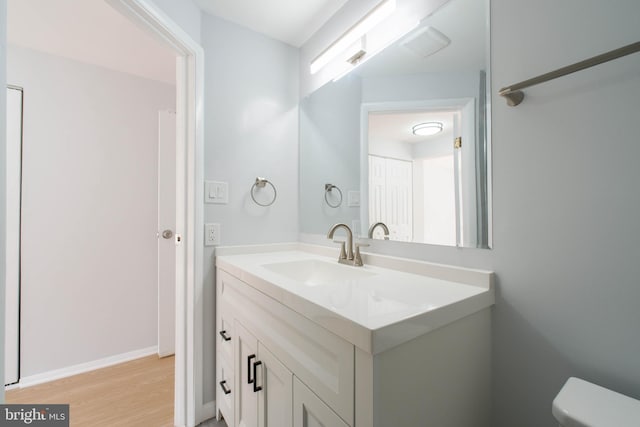 half bath featuring wood finished floors, vanity, and toilet