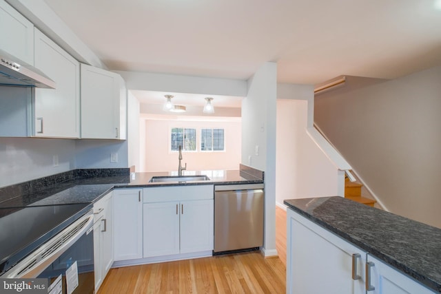 kitchen featuring light wood-style floors, appliances with stainless steel finishes, dark stone counters, and a sink