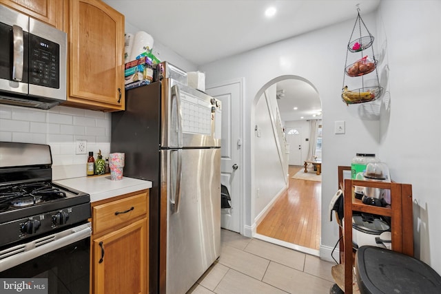 kitchen featuring stainless steel appliances, arched walkways, recessed lighting, decorative backsplash, and light countertops