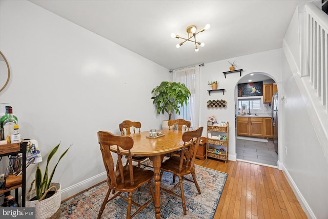 dining area featuring baseboards, arched walkways, light wood-style flooring, and an inviting chandelier