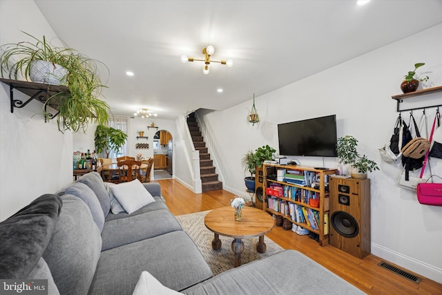 living room with stairway, wood finished floors, arched walkways, a notable chandelier, and visible vents