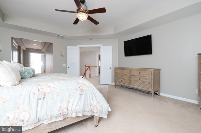 bedroom with light carpet, a tray ceiling, baseboards, and a ceiling fan