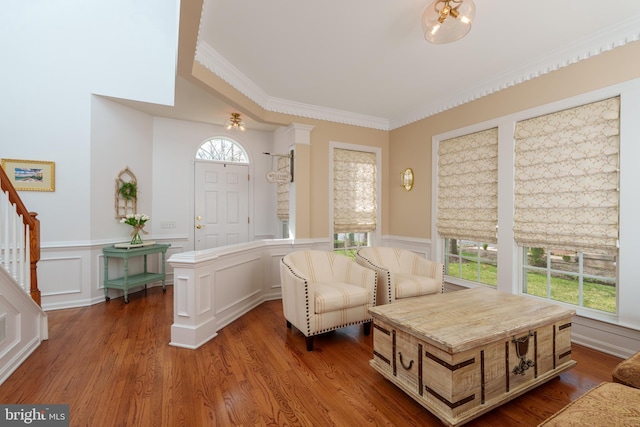 sitting room with a decorative wall, stairway, wood finished floors, wainscoting, and ornamental molding