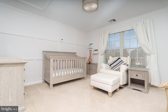 bedroom with a decorative wall, a nursery area, and light colored carpet