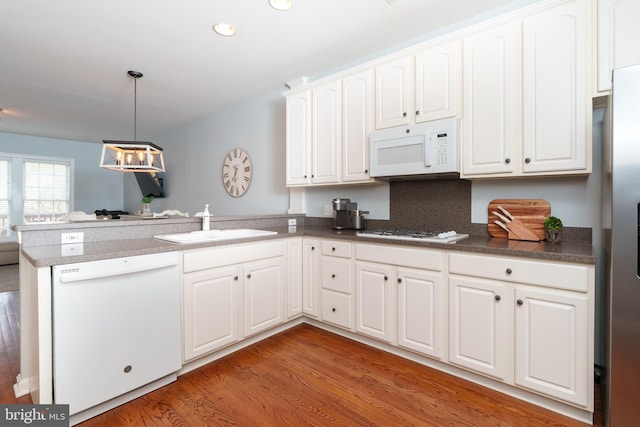 kitchen with white appliances, a peninsula, a sink, white cabinets, and light wood-style flooring