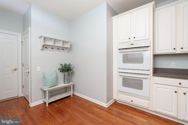 kitchen featuring double oven, dark countertops, light wood finished floors, baseboards, and white cabinetry