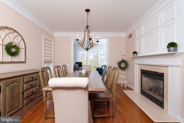 dining room with wood finished floors, ornamental molding, a chandelier, and a fireplace