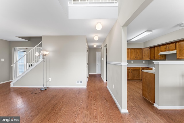 kitchen featuring wood finished floors, brown cabinets, light countertops, under cabinet range hood, and visible vents